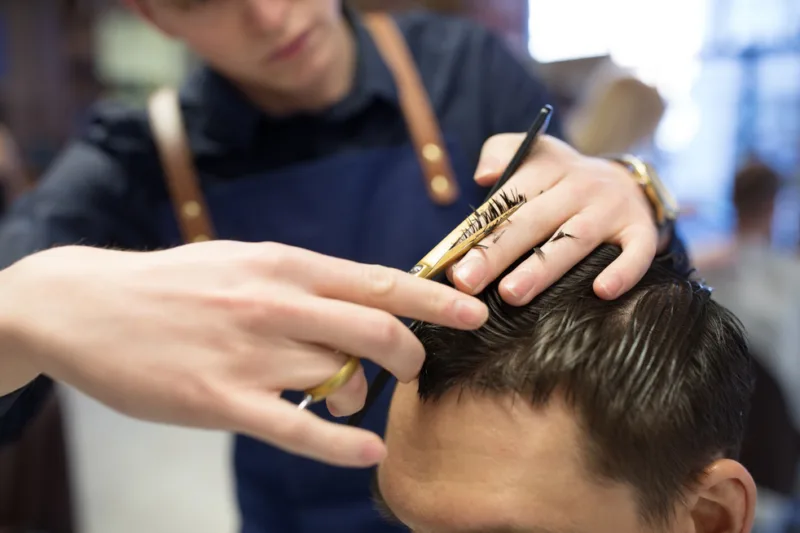 male hairdresser cutting hair at barbershop