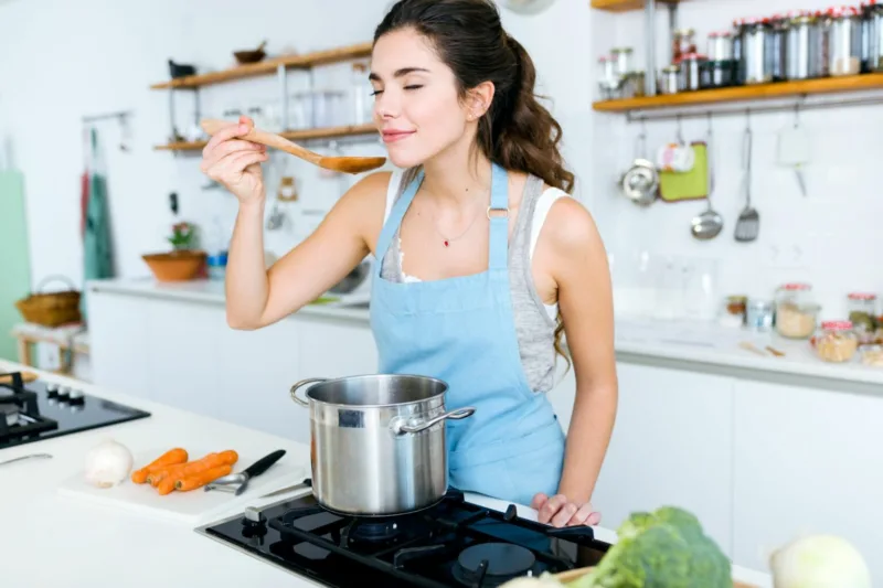 Beautiful young woman cooking soup with vegetables at home.