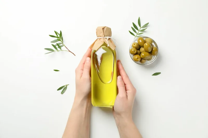 Female hands hold bottle with olive oil on white background, top view