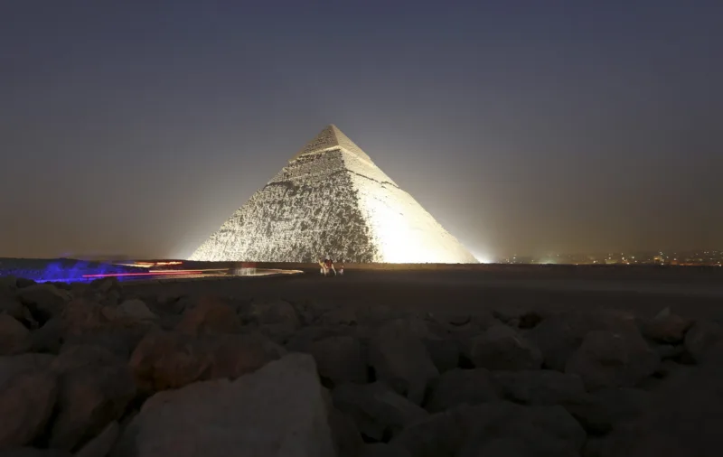 People and a camel stand next to the pyramid of Khufu, during a reopening ceremony of the Sphinx, in Giza