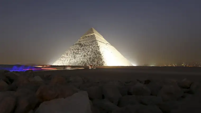 People and a camel stand next to the pyramid of Khufu, during a reopening ceremony of the Sphinx, in Giza