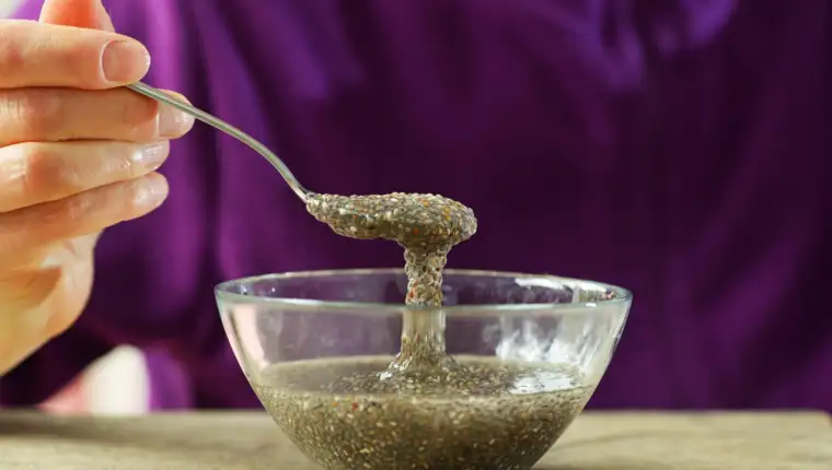 Woman hand with spoon of chia seeds in water