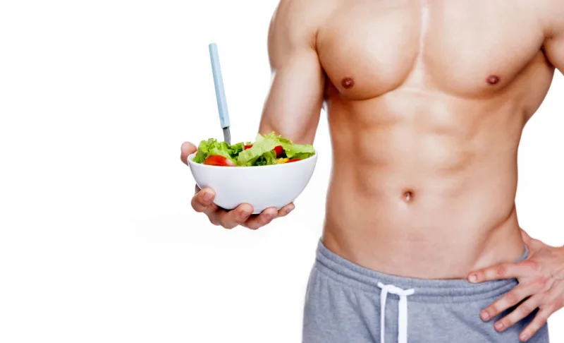 Muscular man holding a bowl of salad, isolated on white backgrou