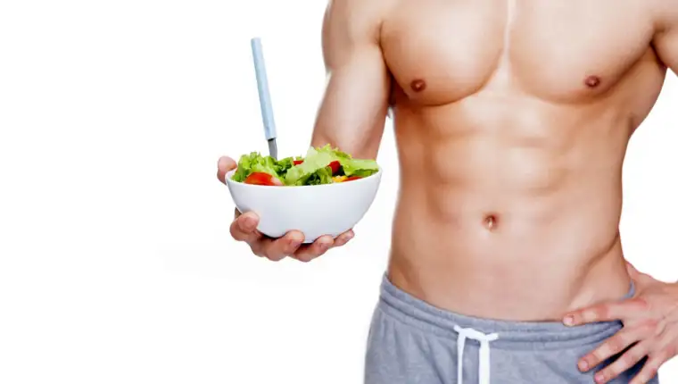 Muscular man holding a bowl of salad, isolated on white backgrou