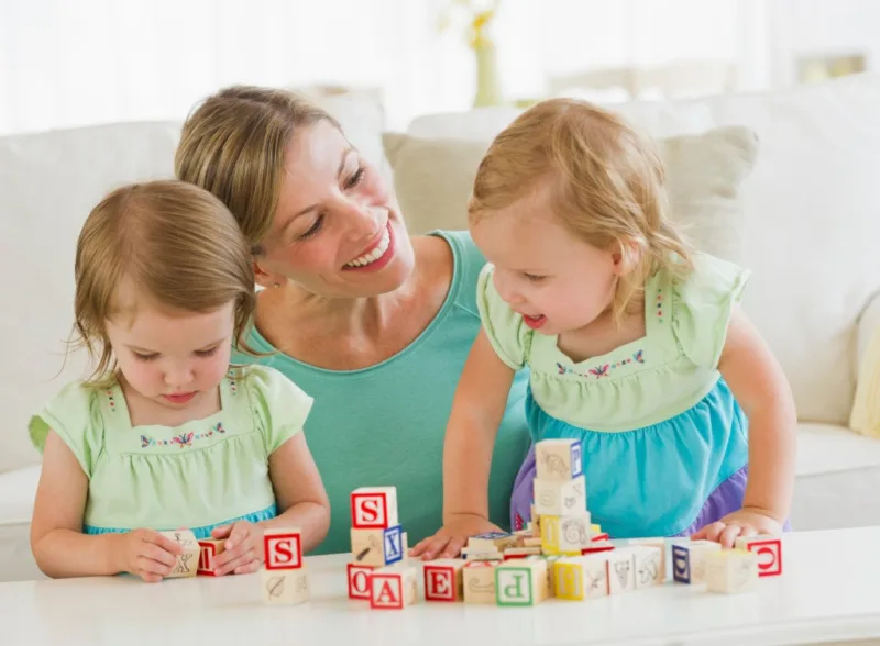Mother and daughters (3-4) playing with letter blocks