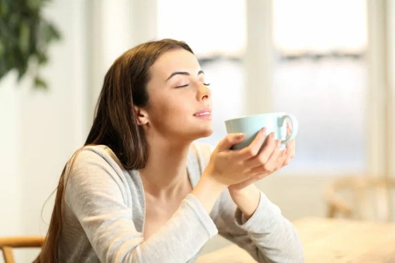 Woman smelling coffee aroma at home