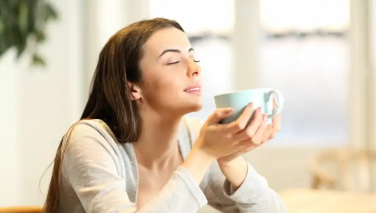 Woman smelling coffee aroma at home