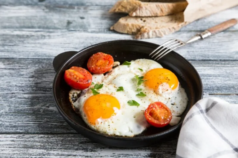 Fried egg. Close up view of the fried egg on a frying pan with cherry tomatoes and parsley