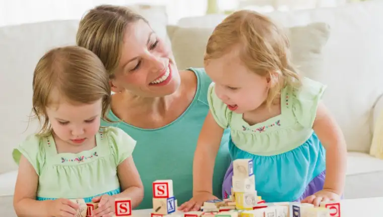 Mother and daughters (3-4) playing with letter blocks