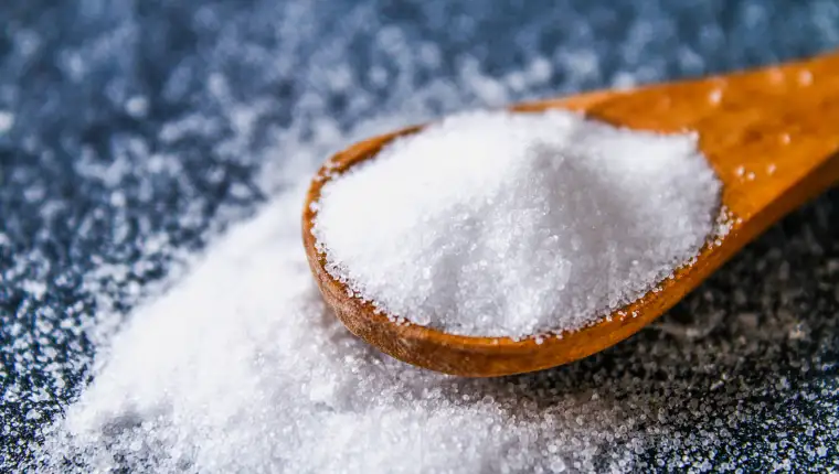 Crystals of shallow salt in a scoop, spoon on a dark gray table. Background for advertising salt. Table salty. Salted food.
