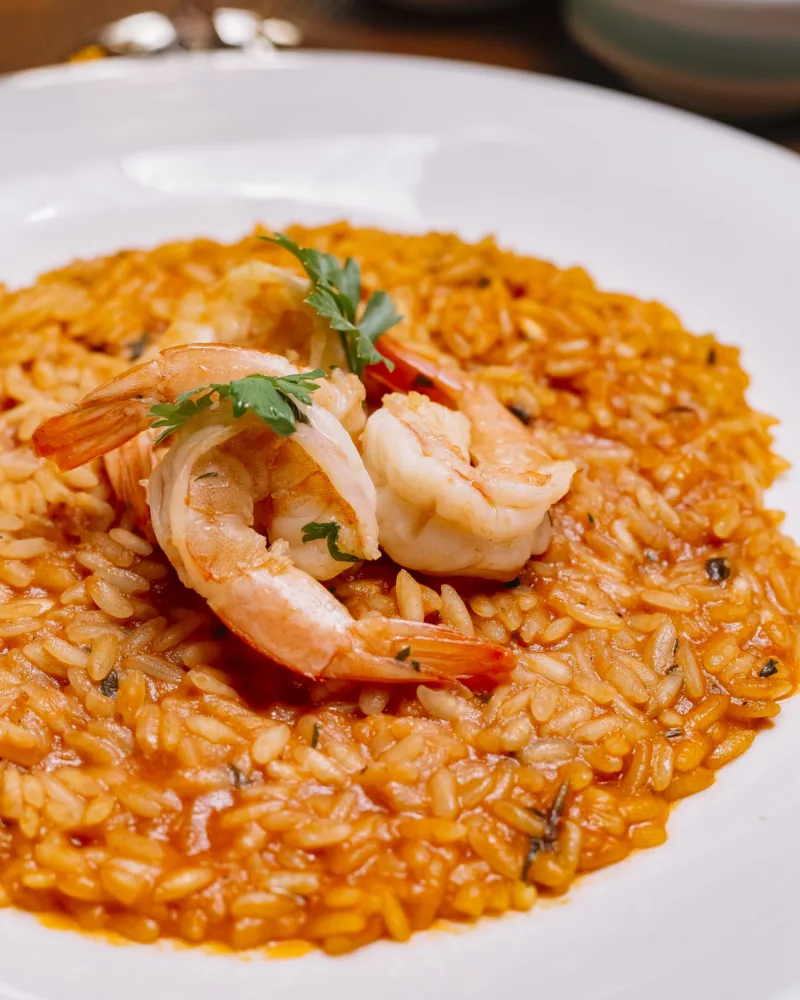 close up of seafood risotto plate with tomato sauce garnished with shrimp