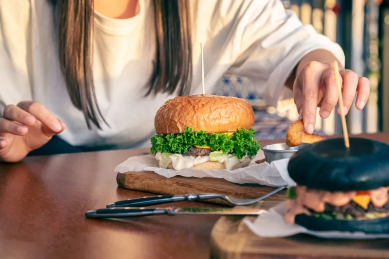 A young woman eating burger in street cafe, close up.