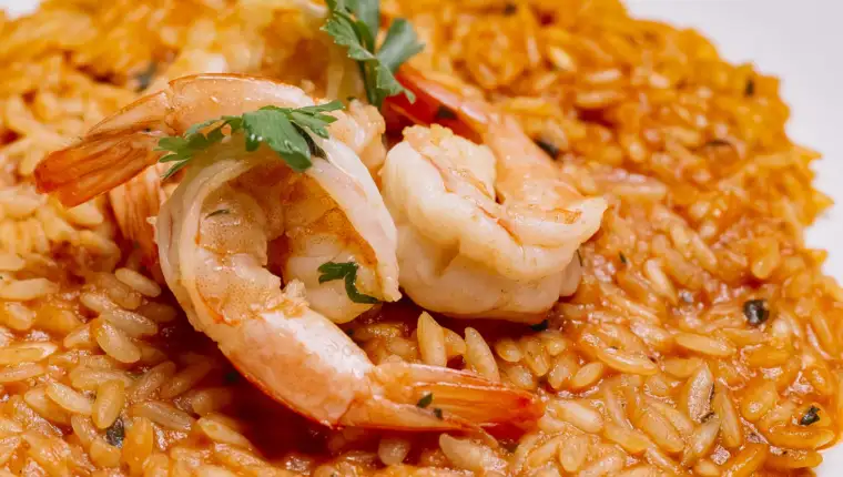 close up of seafood risotto plate with tomato sauce garnished with shrimp