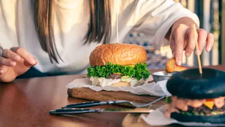 A young woman eating burger in street cafe, close up.