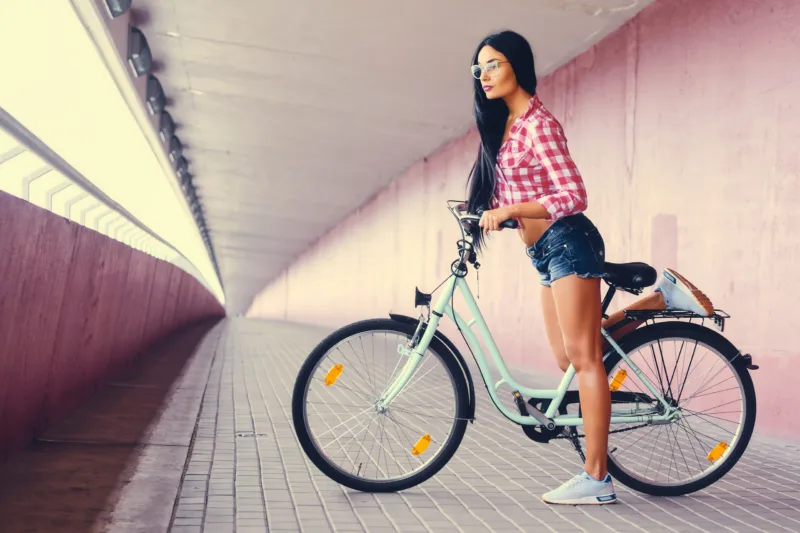 A woman posing on a bicycle in a tunnel with pink walls.