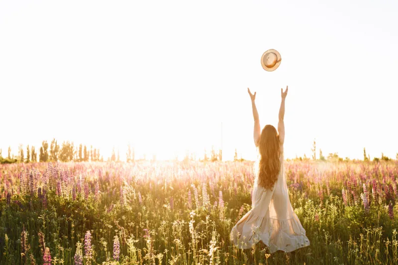 Young woman throw up straw hat in flower field on sunset. Freedom concept, horizontal shot