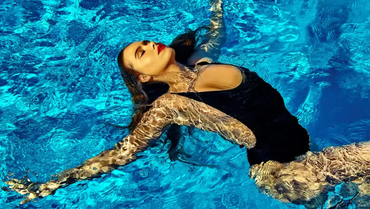 fashion photo of sexy hot beautiful girl model with dark hair in black swimwear swimming on back in pool with red lips