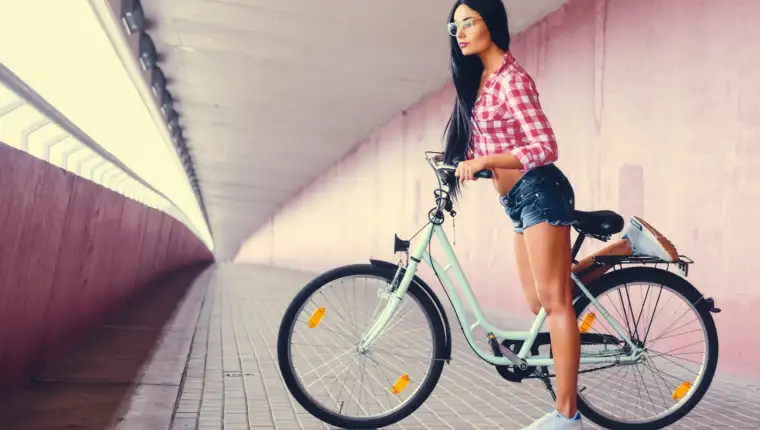 A woman posing on a bicycle in a tunnel with pink walls.