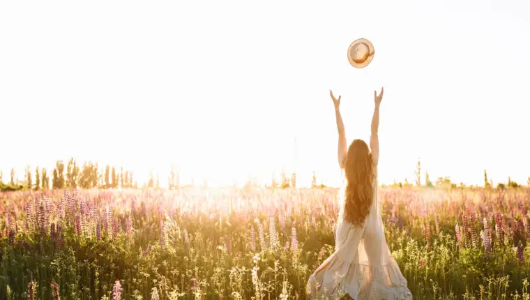Young woman throw up straw hat in flower field on sunset. Freedom concept, horizontal shot