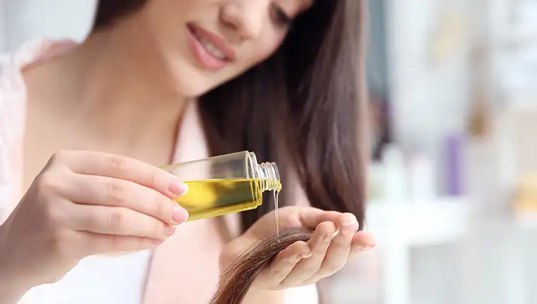 Young,Woman,Applying,Oil,Onto,Hair,At,Home