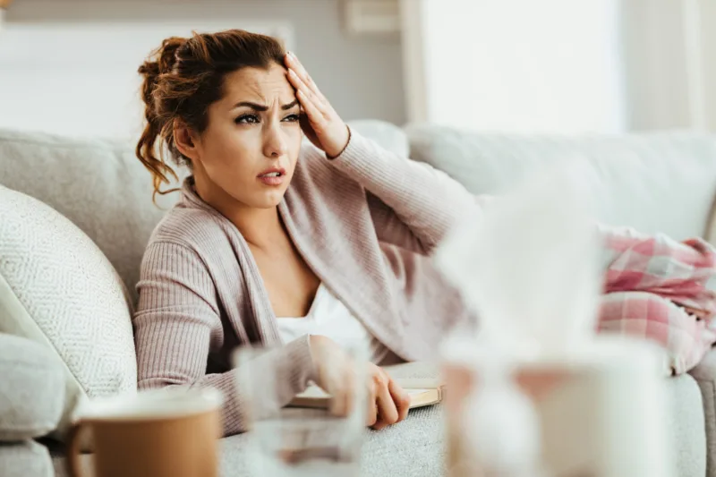 Young woman holding her head in pain while reading book on the s