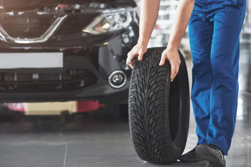 Technician with a blue workwear, holding a wrench and a tire while showing thumb up
