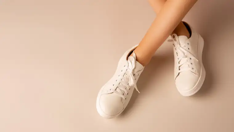 White sneakers shoes and girlâs legs on nude background - casual footwear