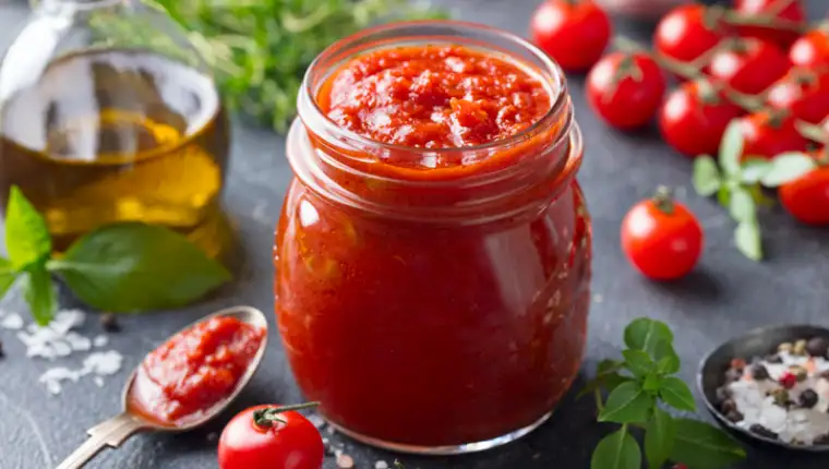 Tomato sauce in a glass jar with fresh herbs, tomatoes and olive oil.