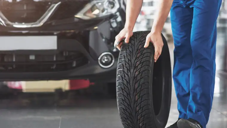 Technician with a blue workwear, holding a wrench and a tire while showing thumb up