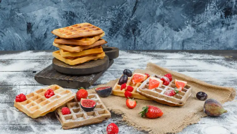 Waffles on wooden board with strawberry,plum,piece of sack on wood with sprinkled flour background, high angle view