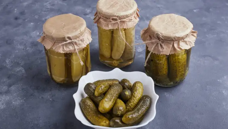 Pickled cucumbers in bowl and glass jars on blue background