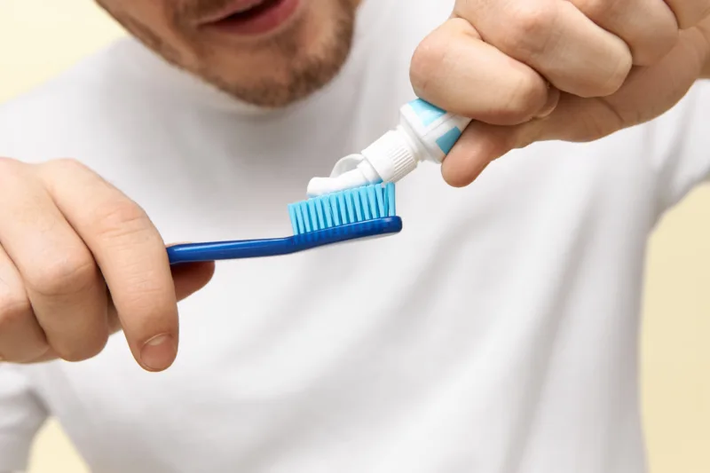 Cropped shot of men's hands holding toothpaste and brush. Unshaven young male squeezing cream dentifrice going to clean oral cavity before sleep. Healthy habits, hygiene and stomatology concept