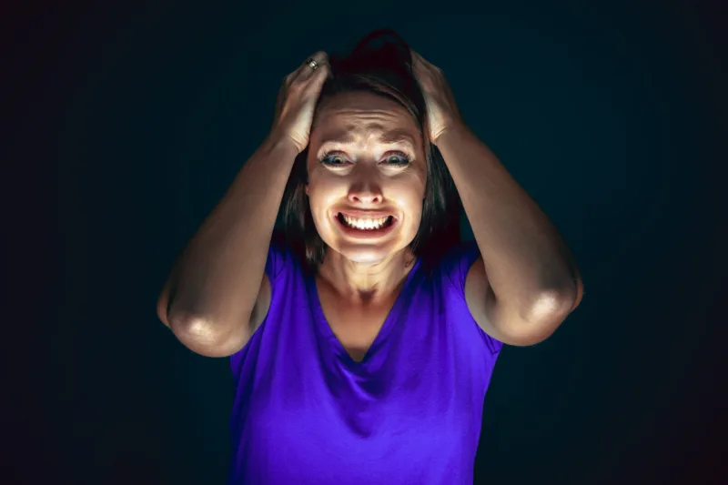 Close up portrait of young crazy scared and shocked woman isolated on dark background