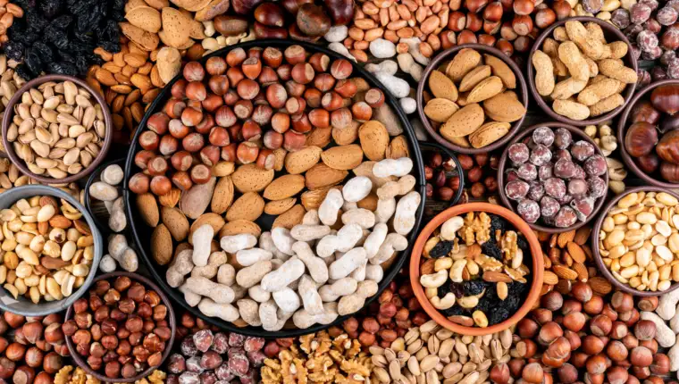Some of assorted nuts and dried fruits with pecan, pistachios, almond, peanut, cashew, pine nuts in a different bowls and black pan flat lay.