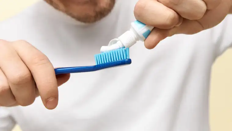 Cropped shot of men's hands holding toothpaste and brush. Unshaven young male squeezing cream dentifrice going to clean oral cavity before sleep. Healthy habits, hygiene and stomatology concept