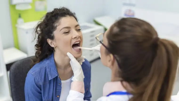 Female patient opening her mouth for the doctor to look in her throat. Otolaryngologist examines sore throat of patient.