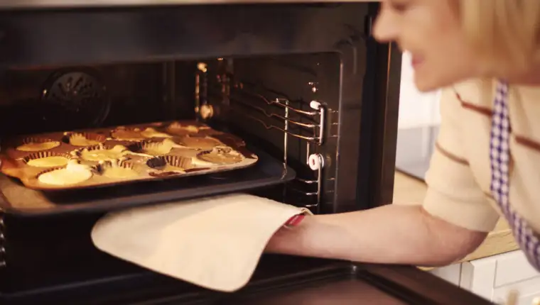 Woman pulls muffins from the oven