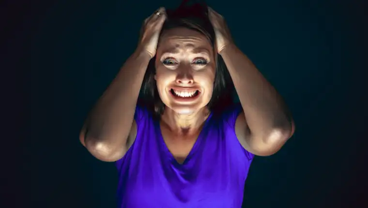 Close up portrait of young crazy scared and shocked woman isolated on dark background