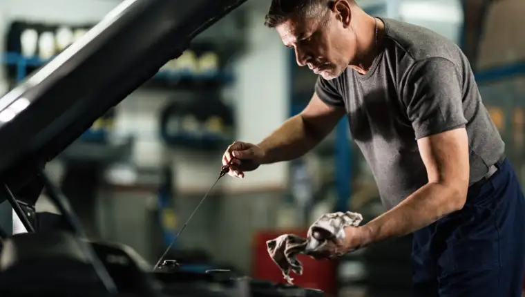 Auto mechanic checking car oil in a repair workshop.