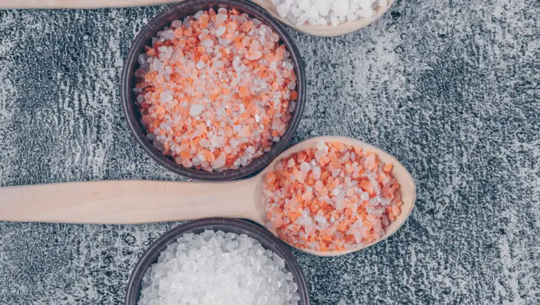 Top view sea salt in bowls and wooden spoons with himalayan salt on gray textured background. vertical