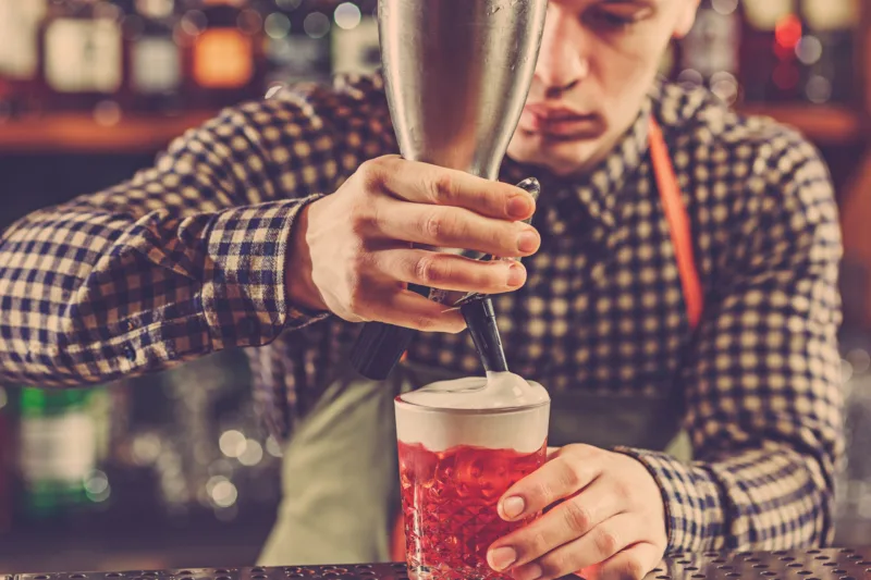 Barman making an alcoholic cocktail at the bar counter on the bar background