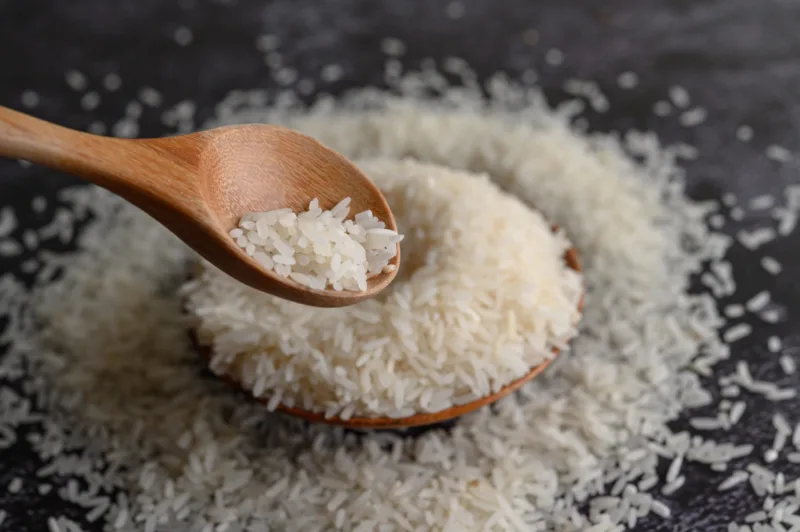 Milled rice in a bowl and a wooden spoon on the black cement flo