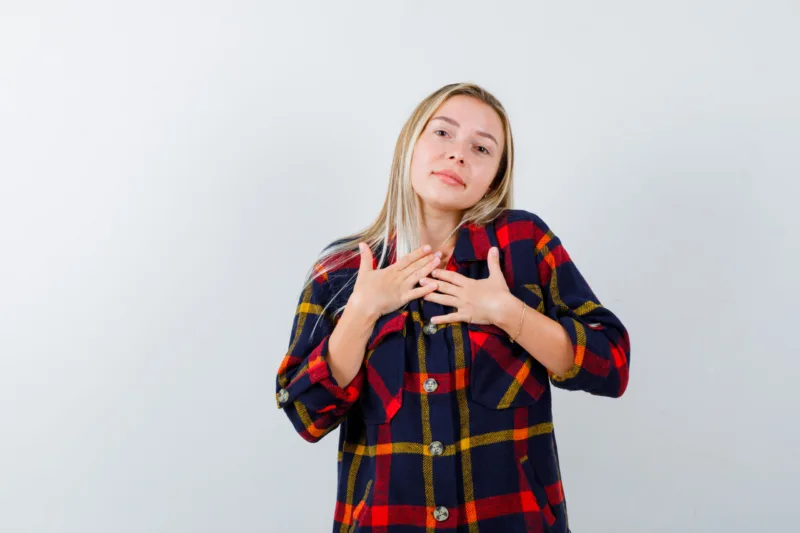 young lady holding hands on chest in checked shirt and looking hopeful. front view.
