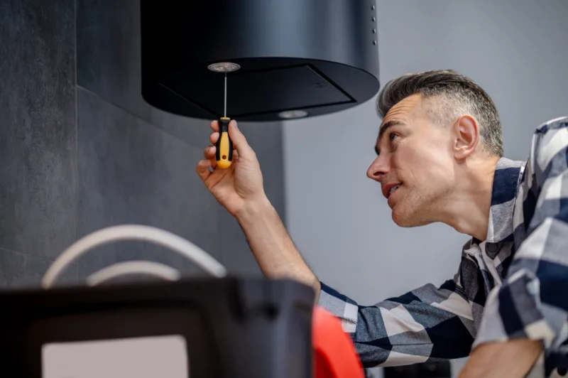 Man with screwdriver twists lamp on kitchen hood