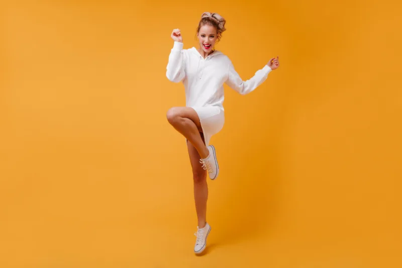 Perky, full of strength lady in good mood is having fun on isolated background. Blonde with curls happily jumping.