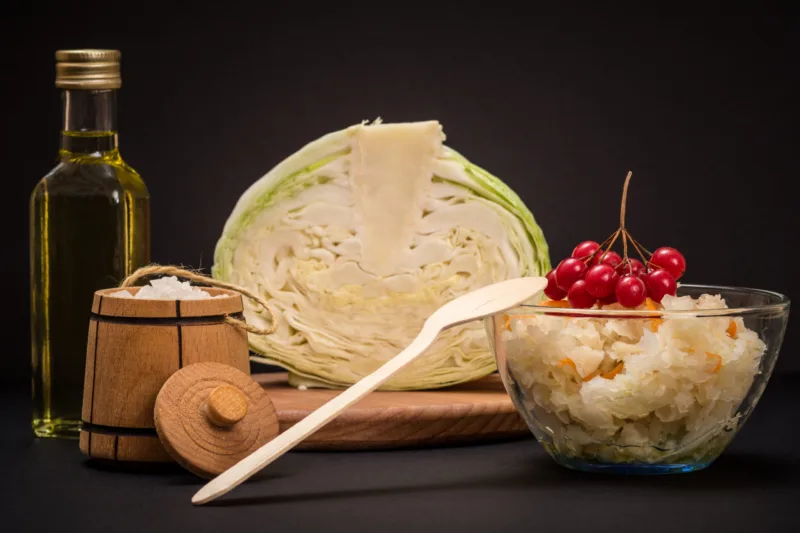 Fermented cabbage with herbs and spices in glass bowl on the black background