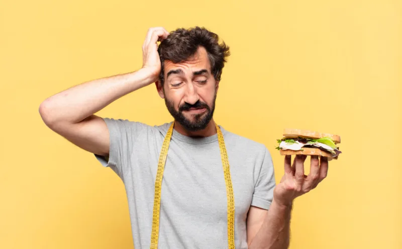 young crazy bearded man dieting sad expression and holding a sandwich