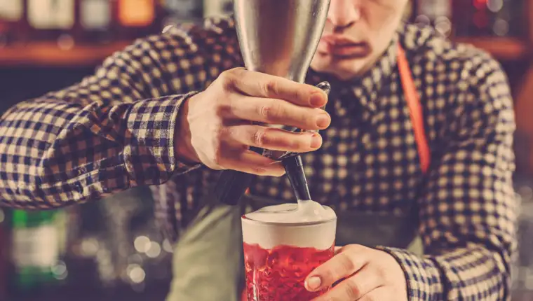 Barman making an alcoholic cocktail at the bar counter on the bar background