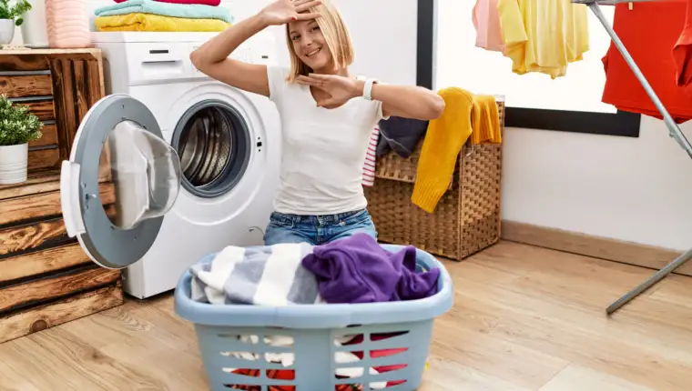 Young caucasian woman doing laundry with clothes in the basket smiling cheerful playing peek a boo with hands showing face. surprised and exited