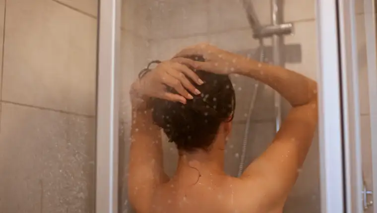 Back view portrait of slime woman with naked shoulders taking shower, posing backwards in bathroom, personal hygiene, morning procedures, hair care and refreshment.